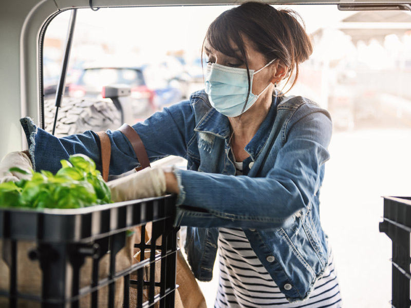 woman with medical mask loading vegetables into van
