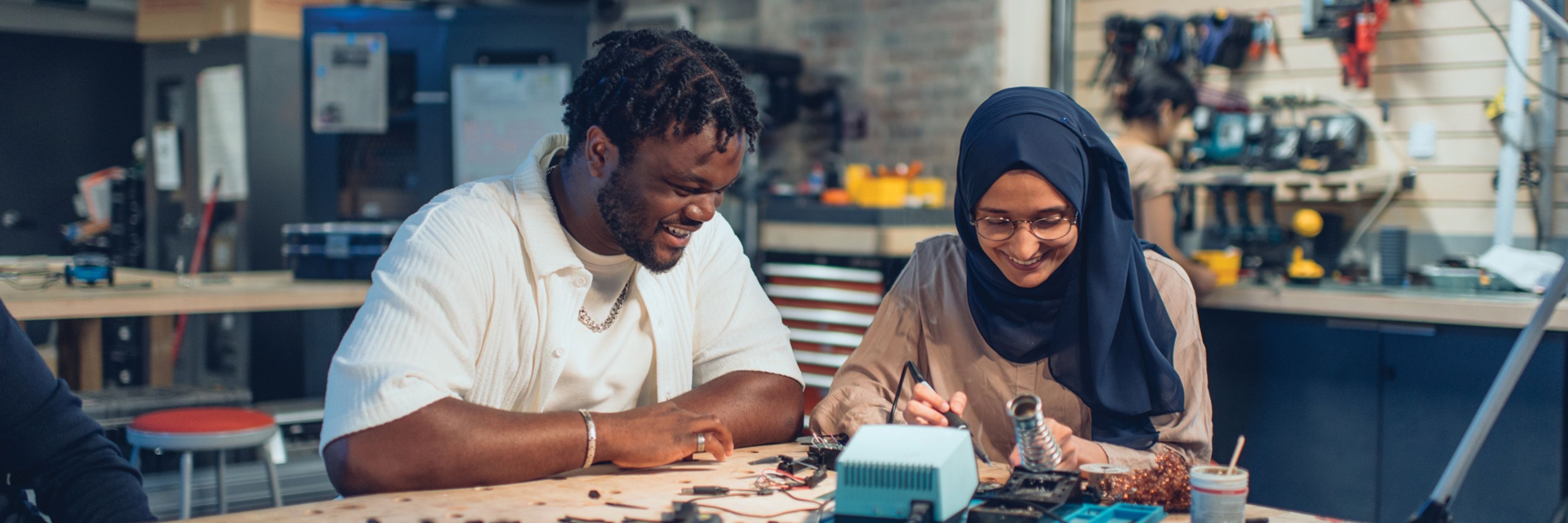 Two students work together at a lab bench, smiling as they assemble an electronic project in a hands-on learning space.