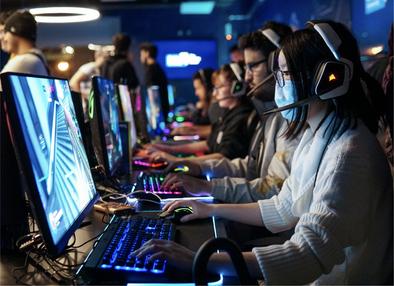 Students playing video games on computers with colourful keyboards and gaming headphones.