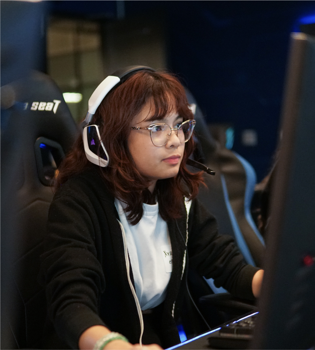 Student with gaming headphones and glasses playing a video game on a computer.