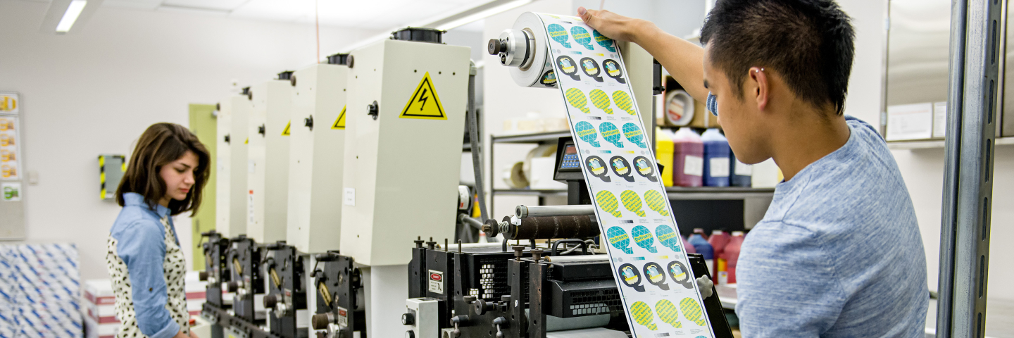 Two students working in a printing facility reviewing a roll of stickers