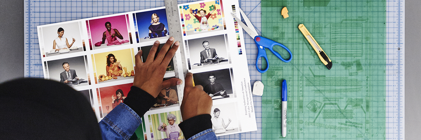 A student working on a printed file with a ruler, scissors and knife. A flexo plate is also on the work table.