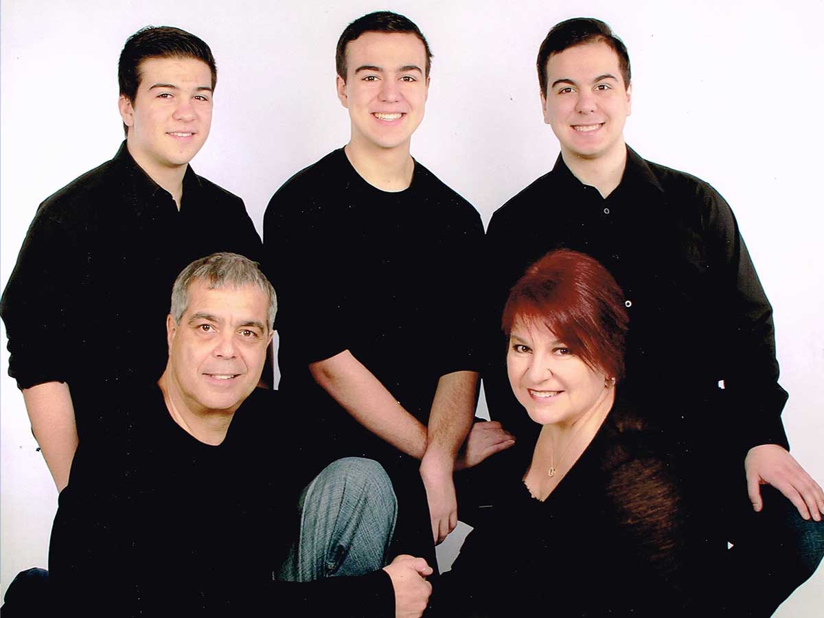 All smiling, three young men kneel behind a man and woman, who are both seated on the floor. 