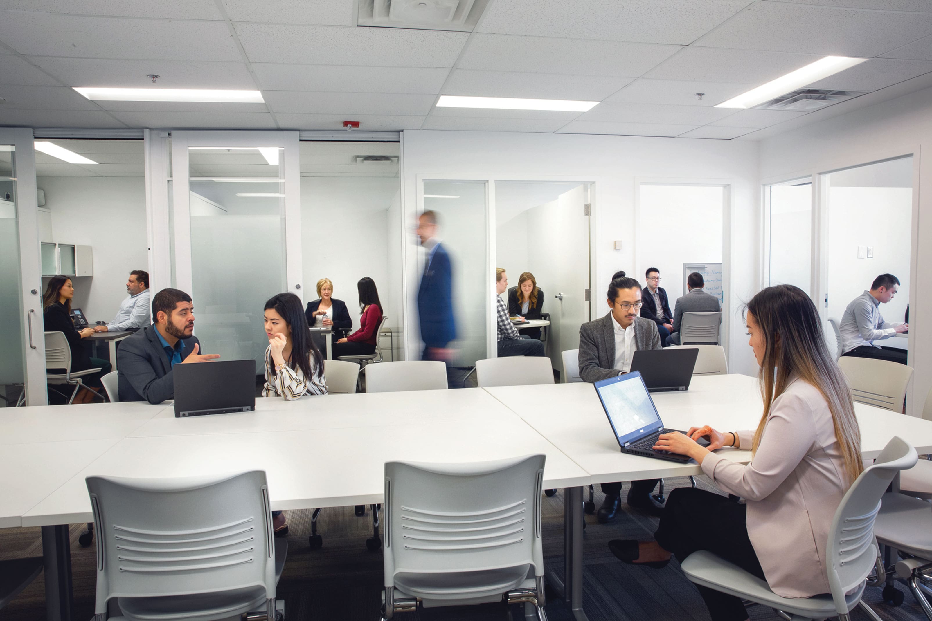 Professionals collaborating in a modern office space with small meeting rooms and open work areas.
