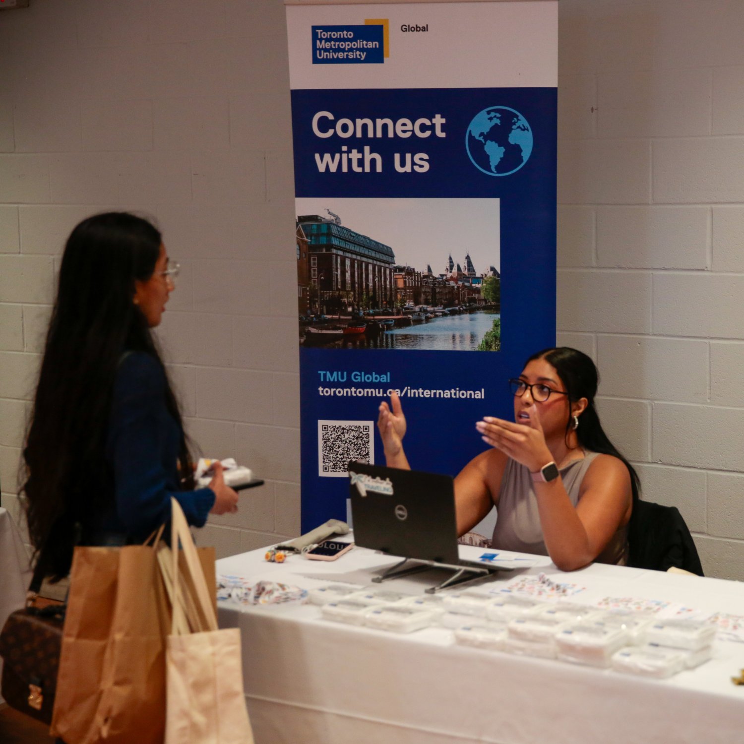 TMU Global booth at an event, with a representative speaking to a visitor.