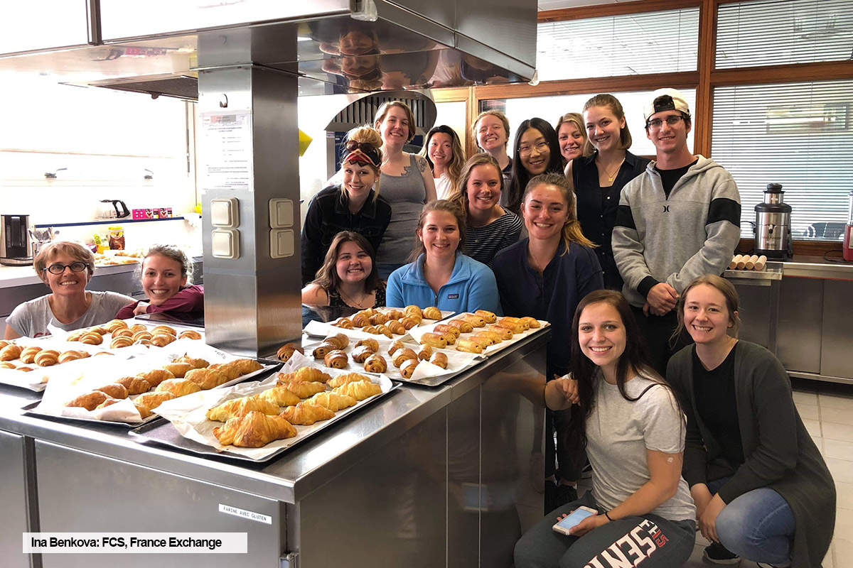 Ryerson FCS student, Ina Benkova, poses with pastries and group of students in a kitchen during a summer course and internship in France.