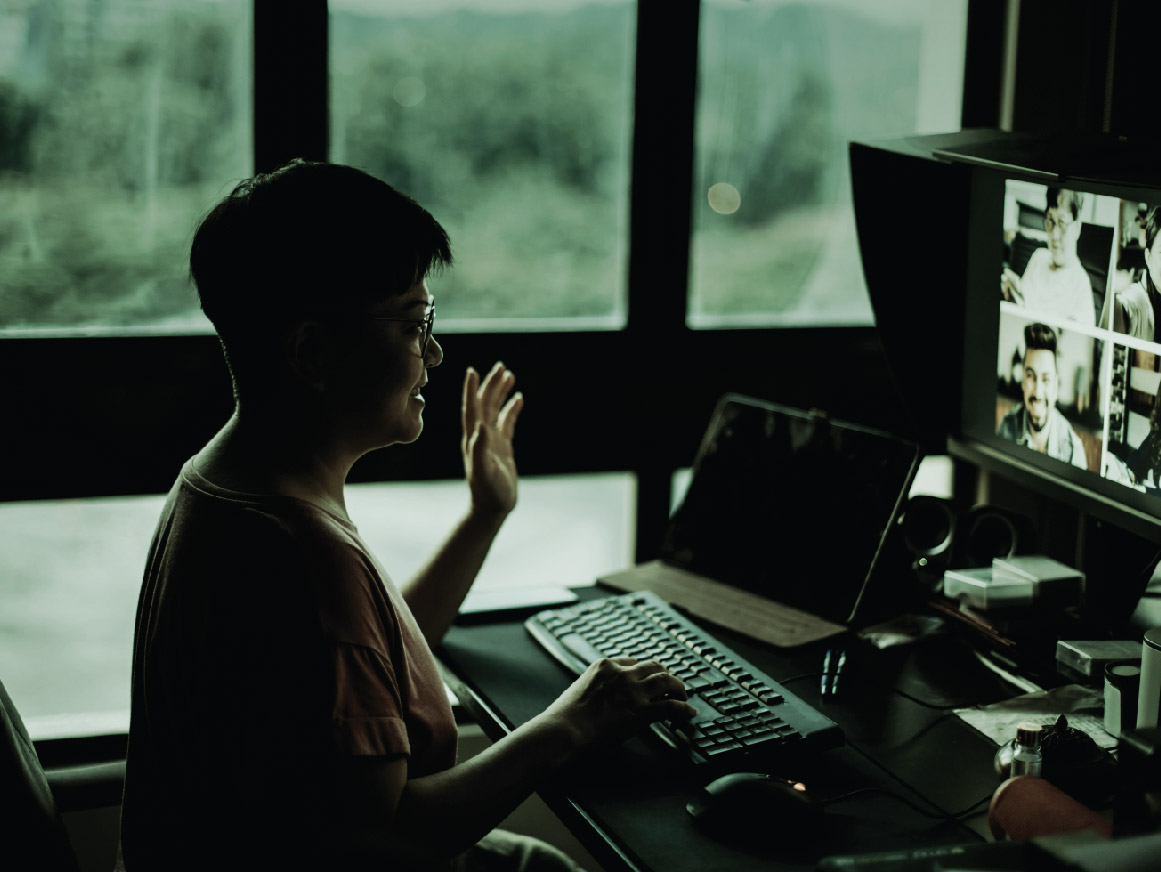 Woman at a desk talking to people virtually on a computer monitor