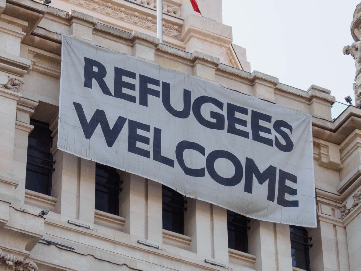 Sign welcoming refugees next to the Spanish flag on the facade of Palacio de Cibeles, Madrid, Spain