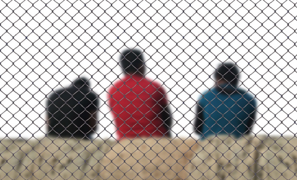 Three men sitting behind a chain link fence