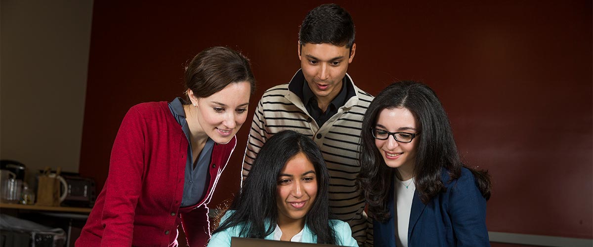 A group of students peer down at a computer.
