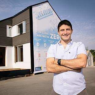 Male grad student standing outside model home