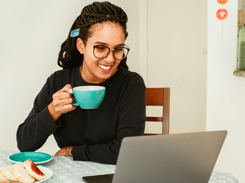 Person holding a mug while using a laptop at a table.