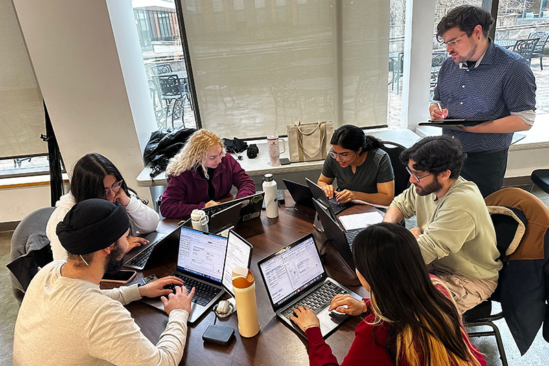 Master of Cybersecurity students working on laptops around a round table