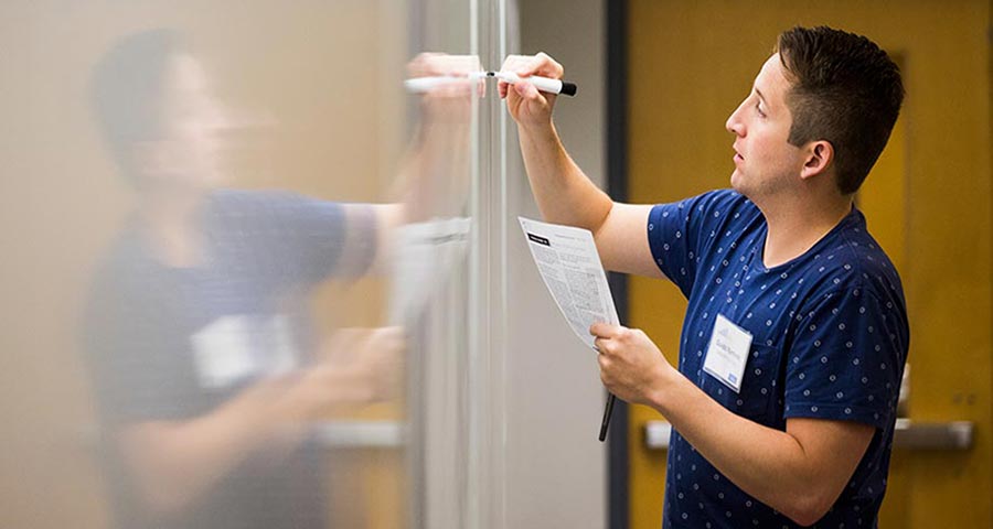 A man holding a piece of paper writes on a whiteboard