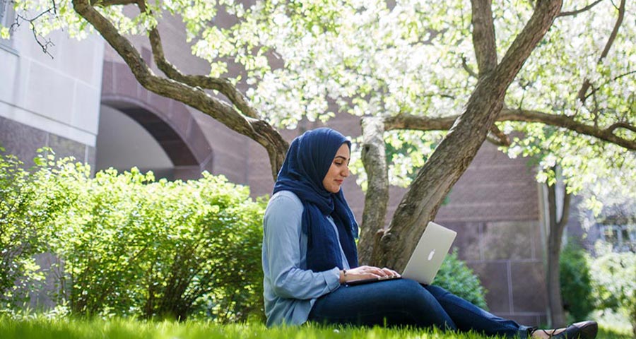 A woman sits with a laptop on her lap in a park