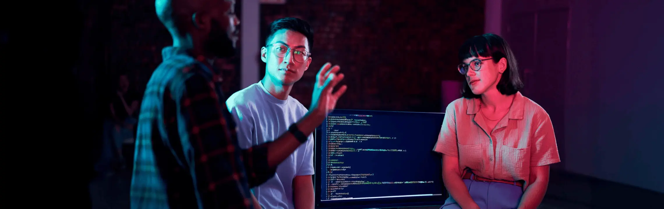 Three graduate students beside a monitor filled with code, bathed in blue and red neon light, creating a tech mood