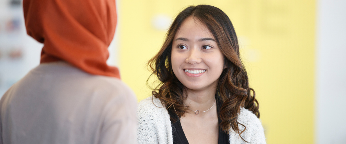 A student smiles at another student with a yellow background.