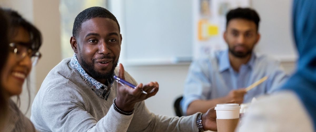 A man holding a pen talking to a coworker at meeting.