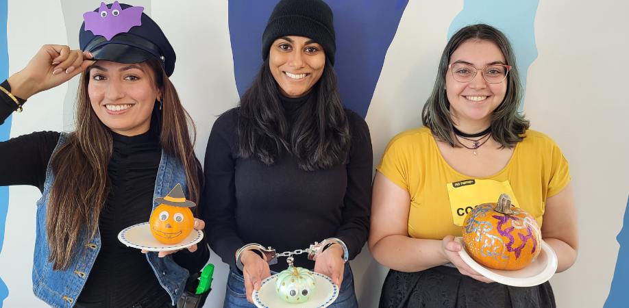 Three female graduate students posed wearing Halloween costumes and holding their painting jack-o-lanterns