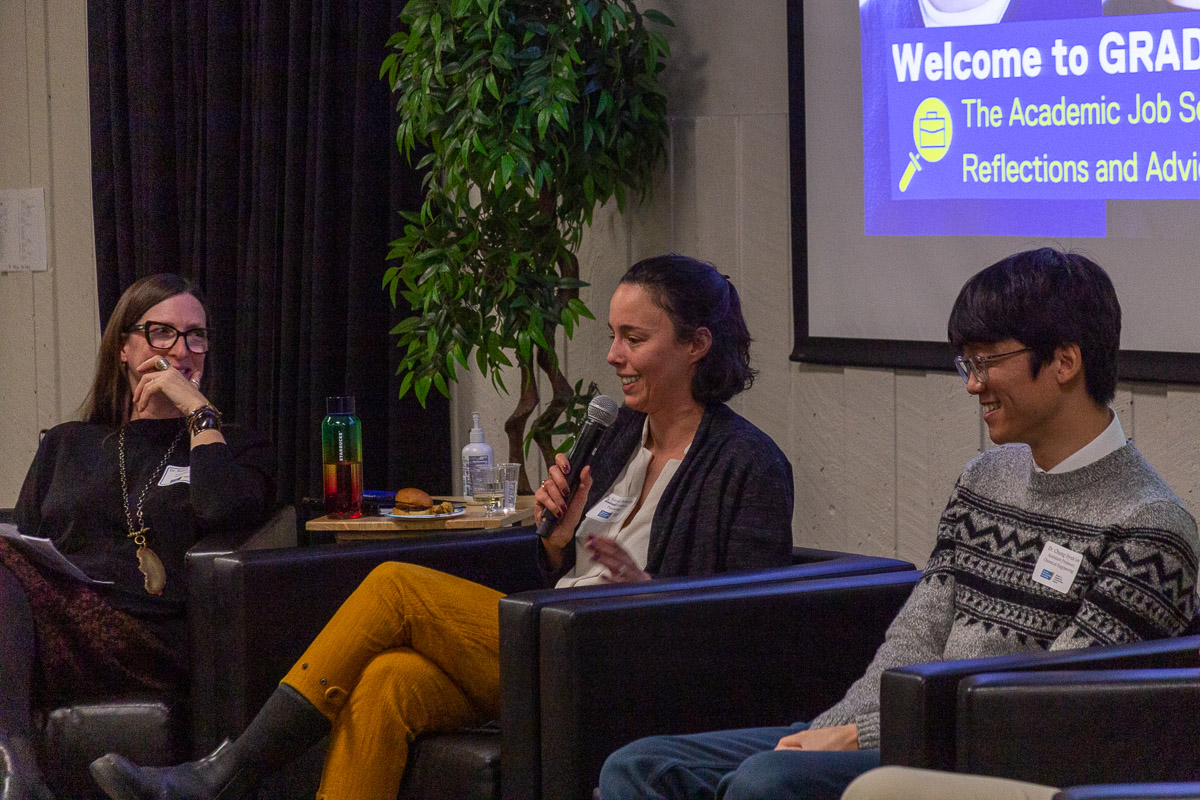 Dr. Sarah Dermody (middle) holds microphone, telling a personal story on stage. Dr. Nancy Walton (left) and Dr. ChungHyuk Lee (right) smiling.