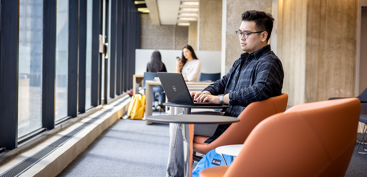 Person sitting in a common area on campus using their laptop.