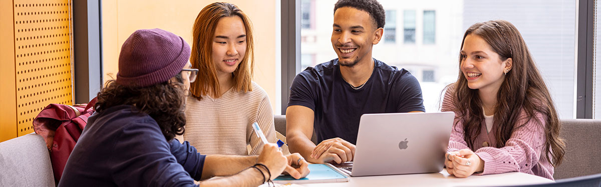 Group of four students collaborating around a computer. 