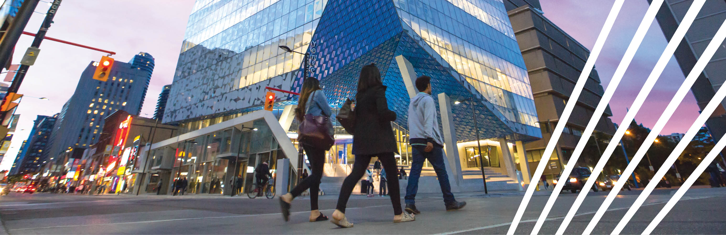 Pedestrians crossing Yonge Street with TMU's Student Learning Centre glowing in the background