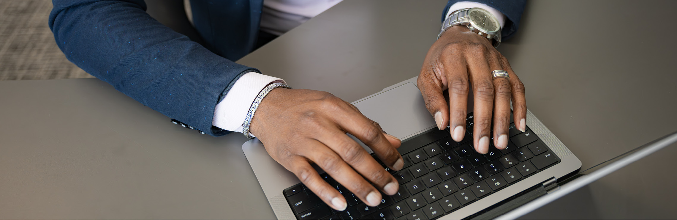Two hands typing on a laptop at a desk.