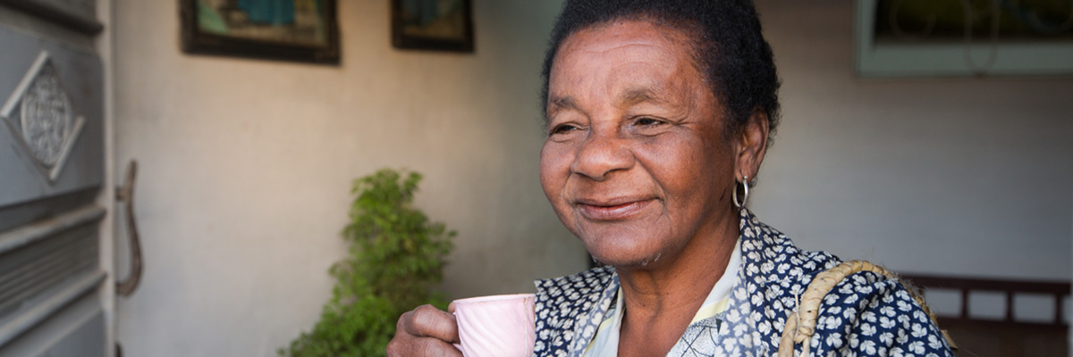 A woman drinking from a pink tea cup smiling.