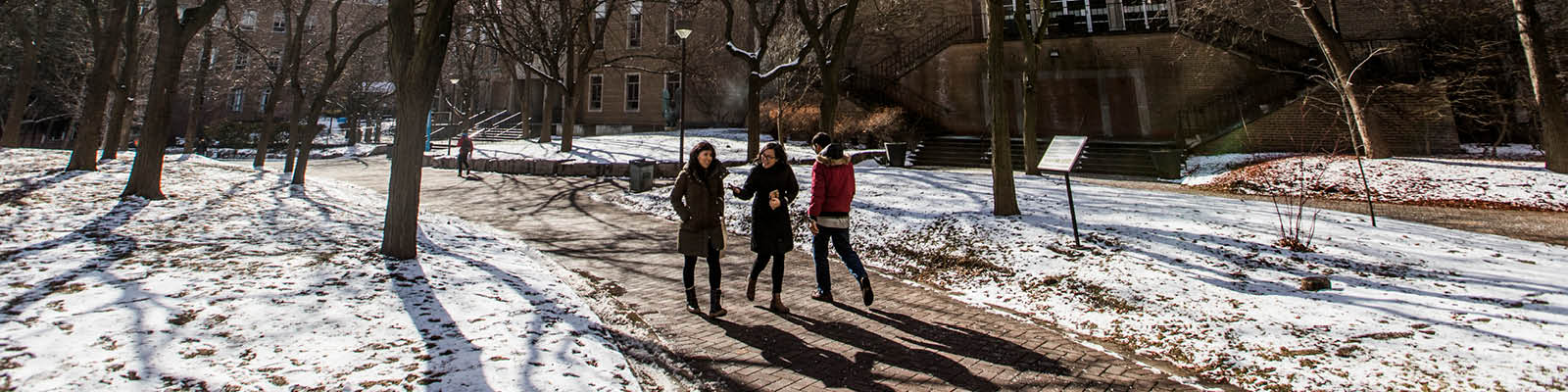 A sunny winter's day on campus. Two three people walking in the snowy Quad.