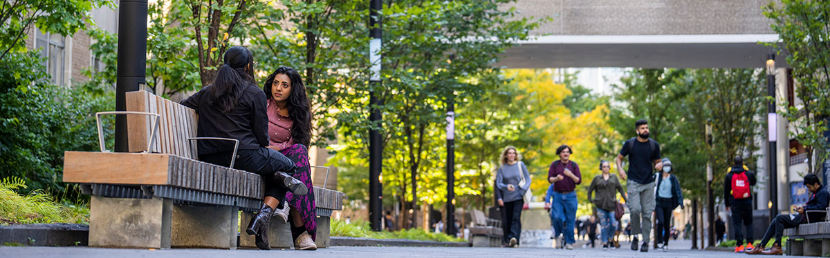 Staff socializing while sitting on bench along TMU's Nelson Mandela Walk.