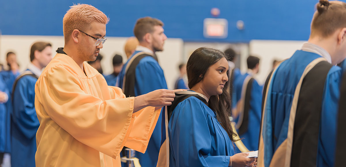 Volunteer helping a student with their gown as they prepare for Convocation