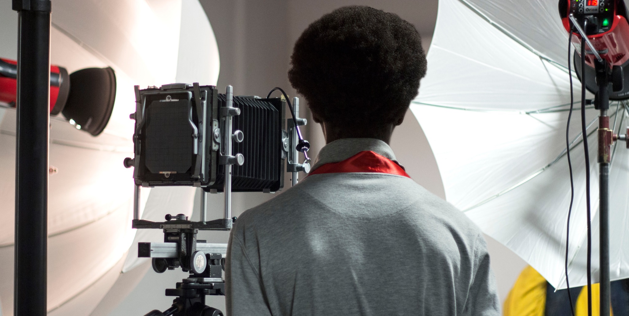 Student in a photography studio standing behind a large format camera with lighting equipment.