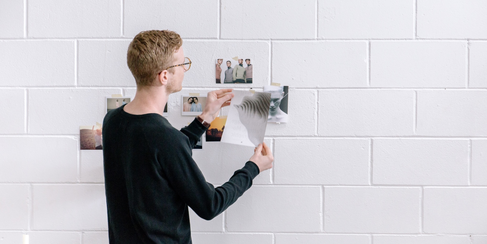 Student arranging prints and photographs on a white wall for display.