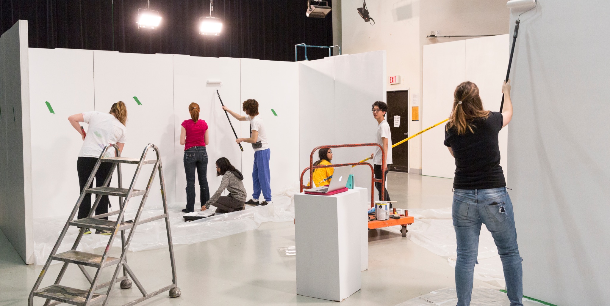 Students working together to paint large white gallery walls.