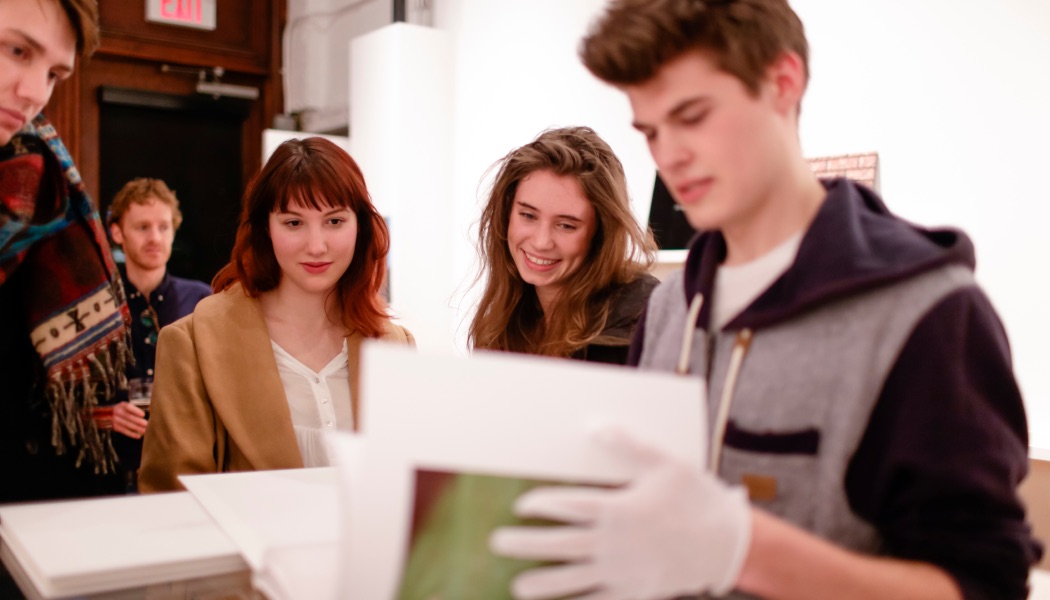 Group of students gathered around prints, examining artwork together.
