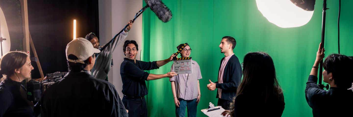 Four students working on a filming production studio with a green screen on the back