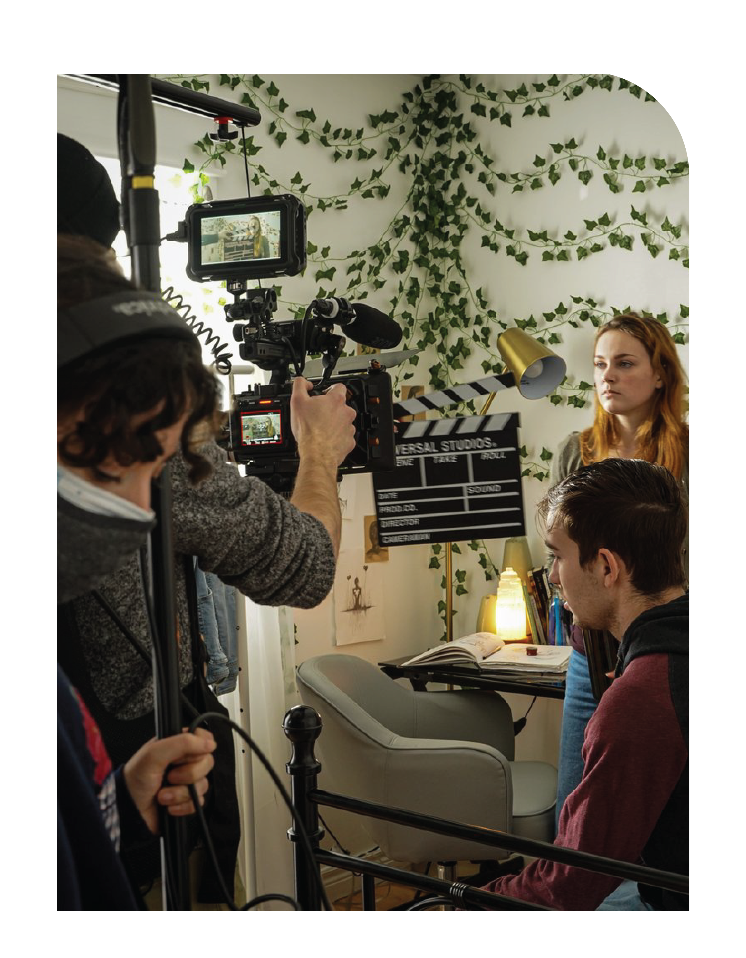 Student holding camera filming actors in a scene