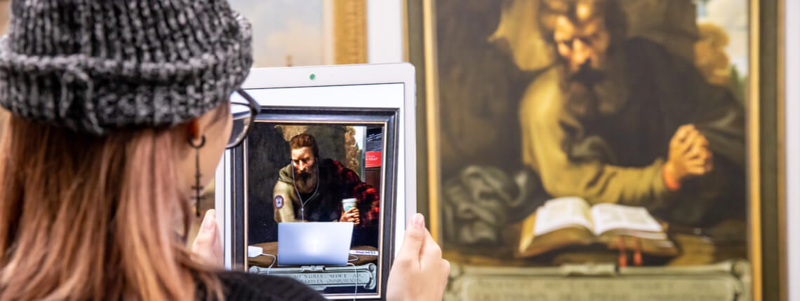 Student holding tablet up to painting to reveal augmented reality experience