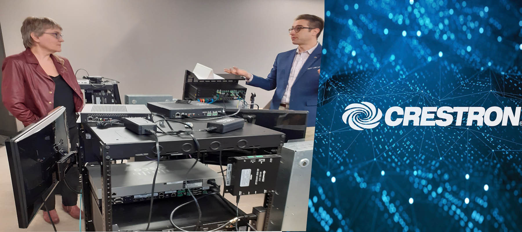 Dr. Fels and Mark Pellegrino converse behind electronic equipment with the Crestron logo on the right