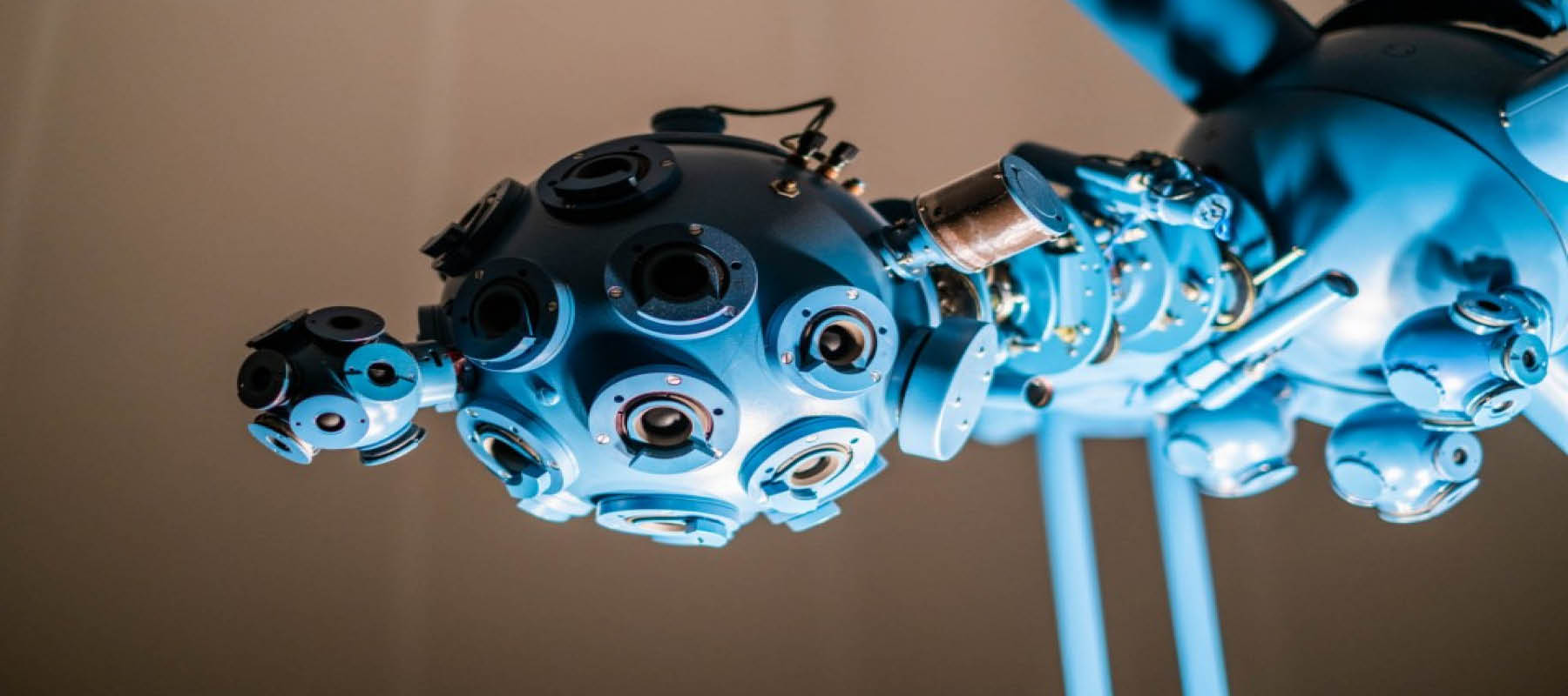 A light blue bulbous technology is covered in black circular protruding camera like objects