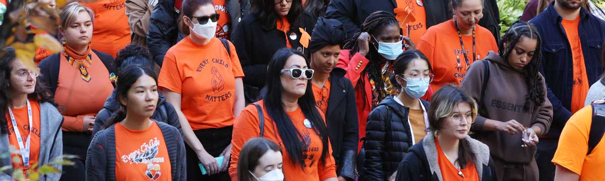 A group of people standing wearing orange shirts with print stating every child matters