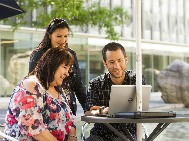 Three Indigenous community members in conversation, looking at a laptop on Gould Street