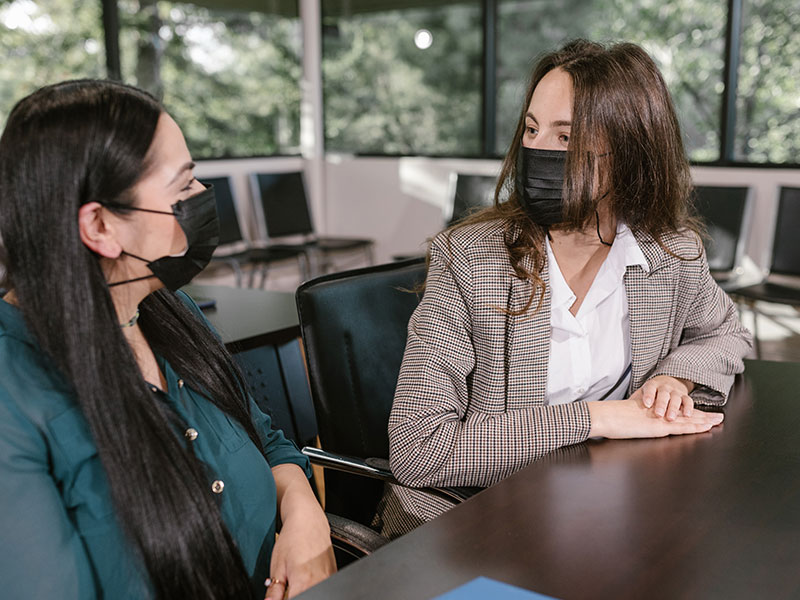 Two people with mask on having a conversation at a table