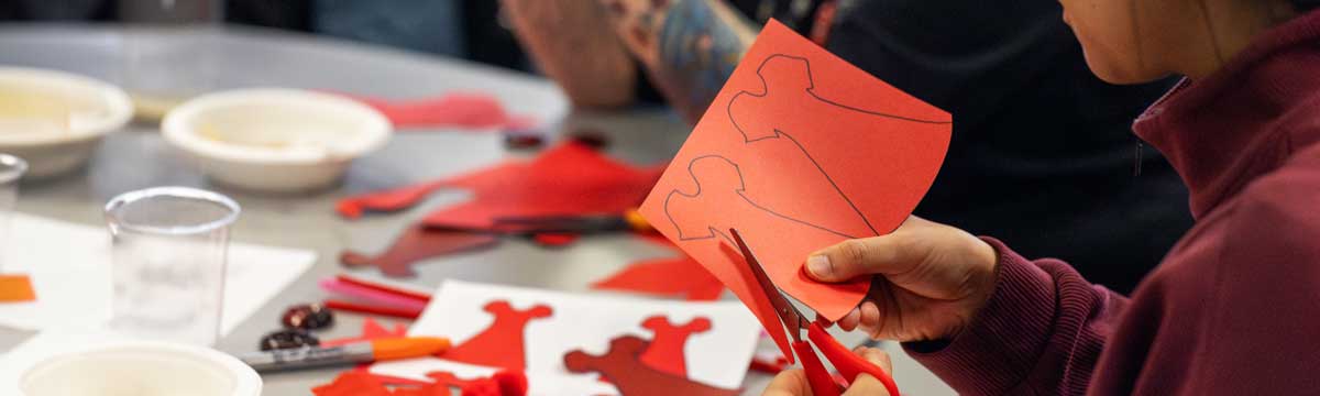 A person cutting out a red dress from red construction paper.