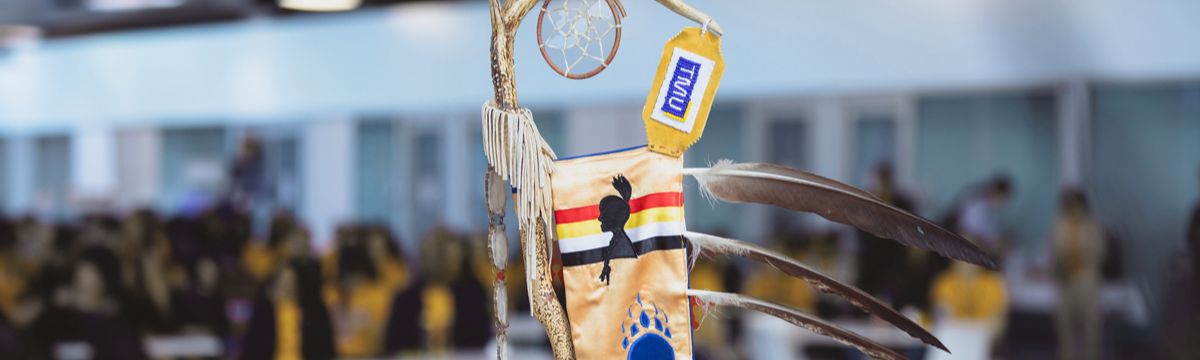 Part of the Eagle Staff, including beaded TMU letters, three feathers and red, yellow, white and black ribbons