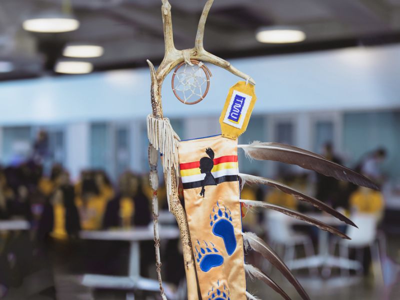 Part of the Eagle Staff, including beaded TMU letters, three feathers and