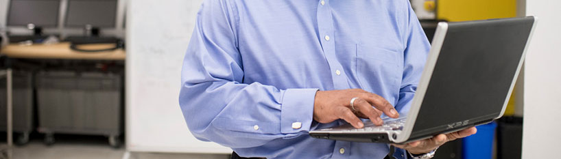 A man holds a laptop with one hand and types with the other.