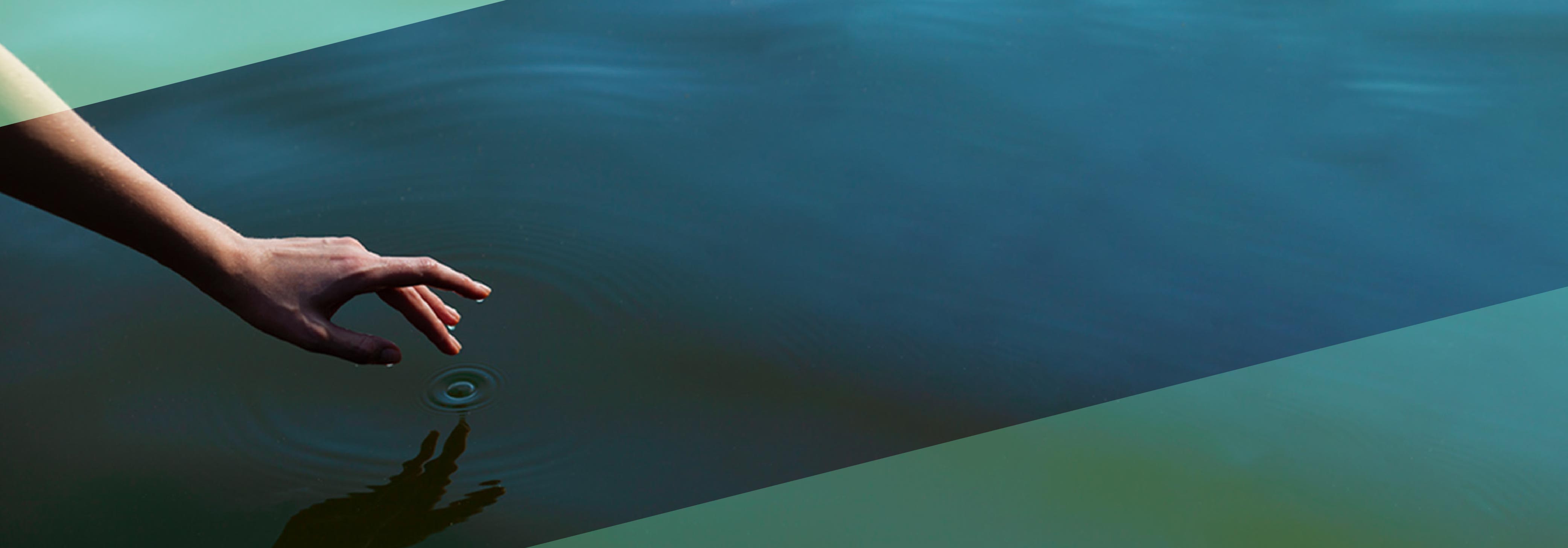 An image of a woman's hand gently touches the water in the pond with green triangles overlaid in the top-left and bottom-right corners
