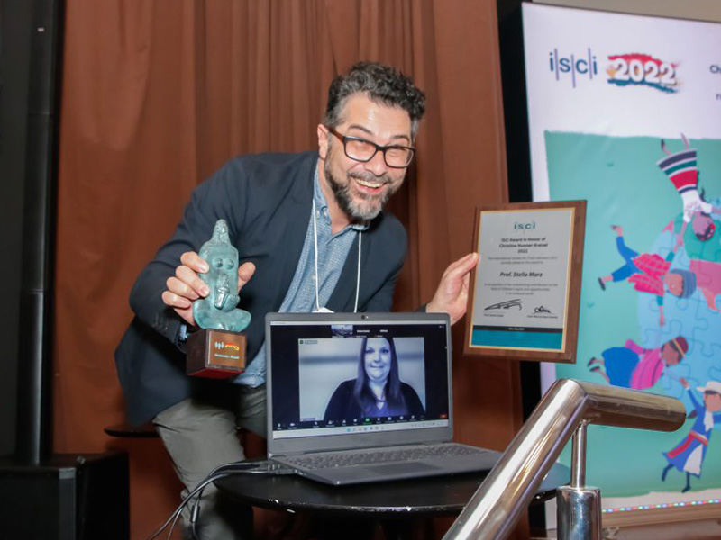 Someone receiving an award on behalf of Stella Marz as Stella Marz is displayed on a computer screen